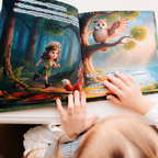 A child reads the personalized children's book "Child: Animal Helper," showing a colorful illustrated spread of a cartoon girl in a ranger outfit running through a dark forest with a fox on the left page, and a worried owl perched on a sunlit tree on the right page.