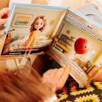 A child reads the personalized children's book "Child Counts to 20," showing a colorful illustrated spread featuring a cartoon girl in a yellow dress and a cheerful talking red balloon character in a cozy bedroom setting.