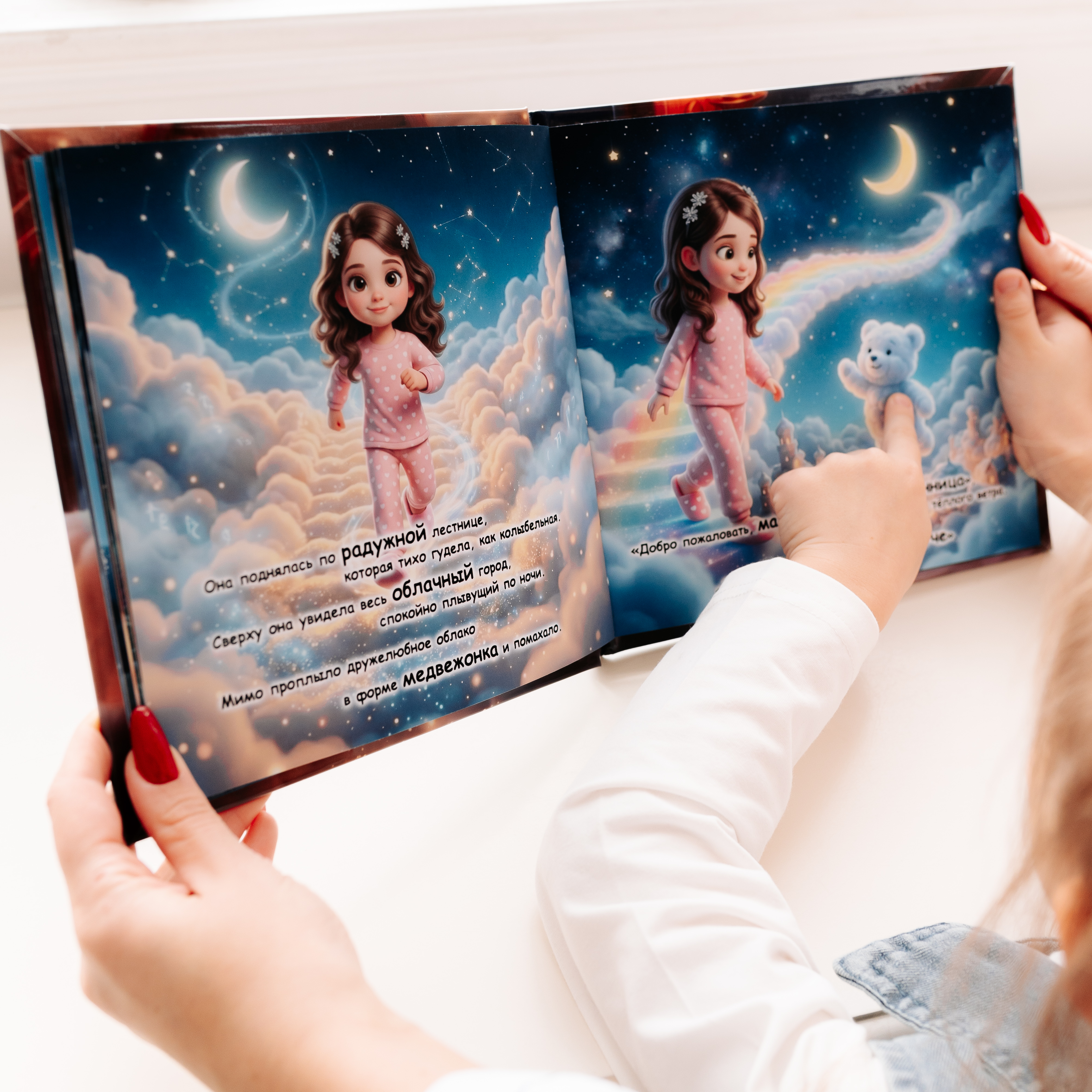 A person holds open the personalized children's book "Child's Dream-Train Adventure," showing a colorful illustrated spread of a dark-haired girl in pink pajamas walking up a rainbow staircase through clouds under a crescent moon, with a fluffy bear cloud companion on the right page.