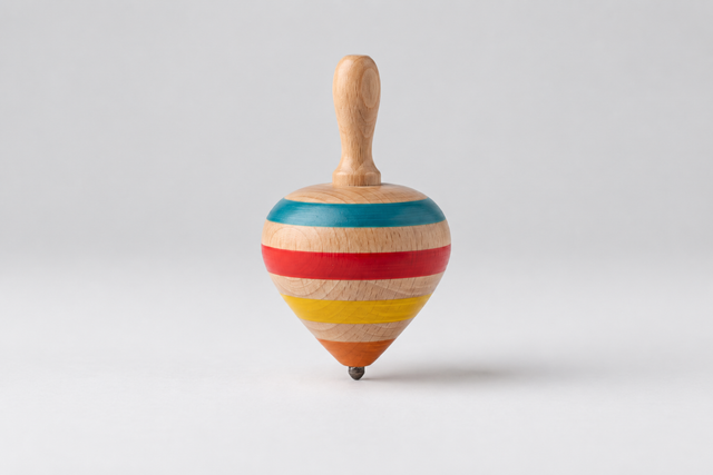 A wooden spinning top toy with horizontal painted stripes in blue, red, beige, yellow, and orange, featuring a natural wood handle and a small metal tip, photographed on a light gray background.