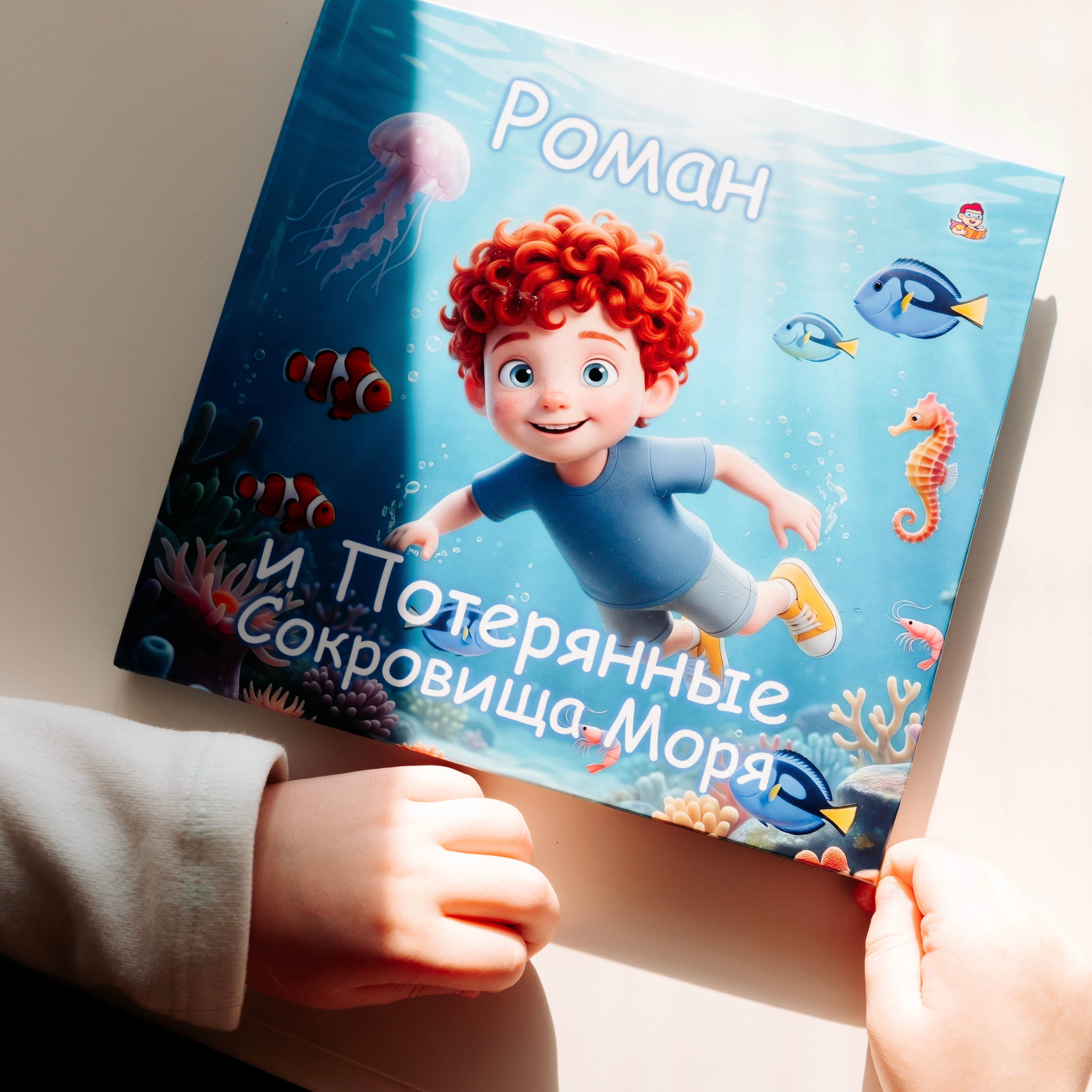 A child holds the personalized children's book "Roman and the Lost Treasures of the Sea," showing a cover with a 3D-illustrated red-haired curly boy swimming underwater among clownfish, blue tangs, and a seahorse above a colorful coral reef.